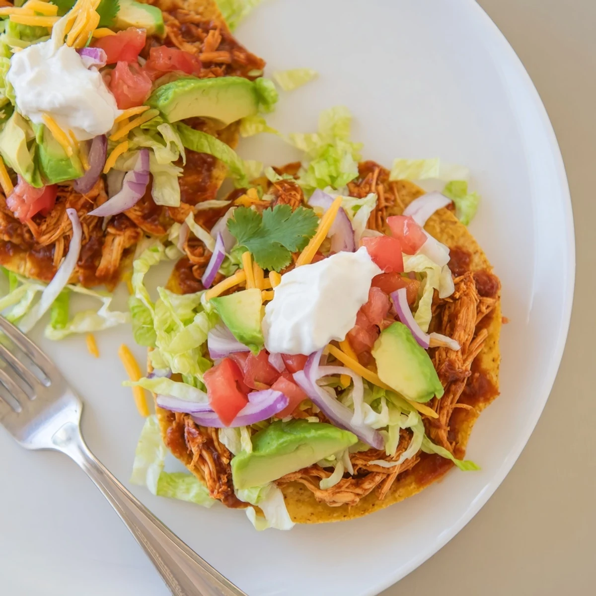 Crispy sweet smoky BBQ chicken tostadas loaded with fresh lettuce, tomato, and creamy avocado slices