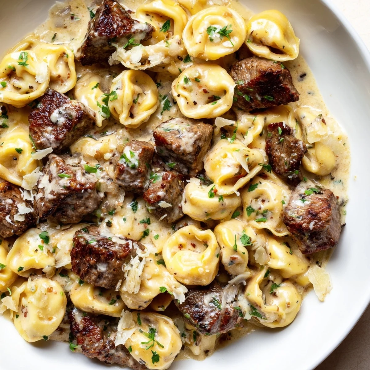 Cheesy tortellini and golden steak pieces swimming in a rich garlic cream sauce