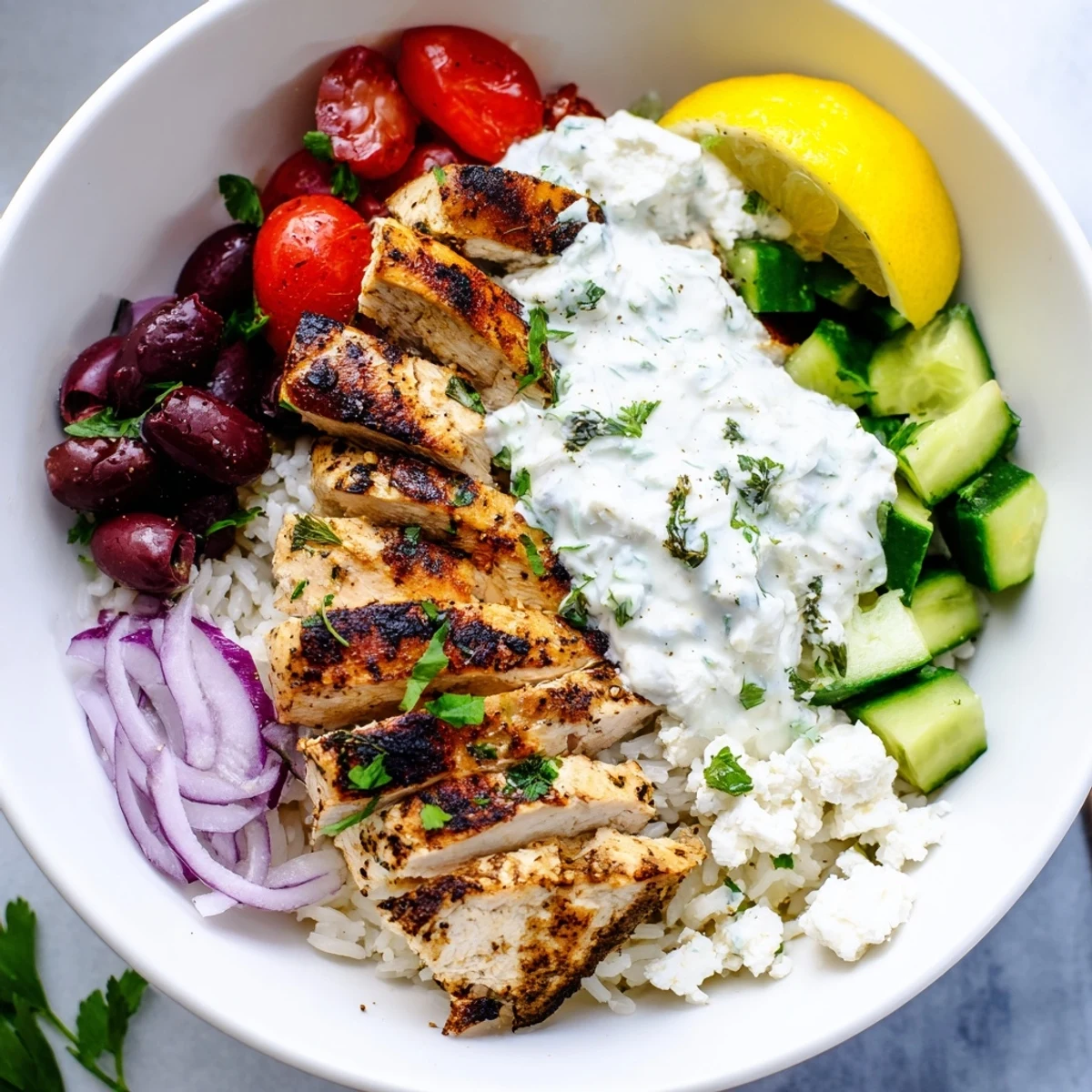 Colorful Greek Chicken Bowls layered over fluffy rice with crumbled feta and olives