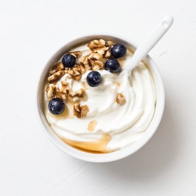 Thick strained Greek yogurt spoon drizzling golden honey over granola and sliced strawberries