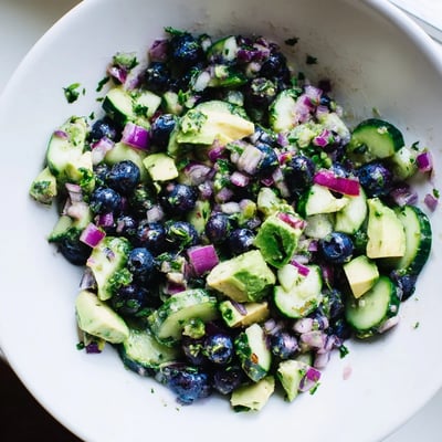 Close-up of fresh blueberry cucumber salsa spooned over grilled fish on a white plate