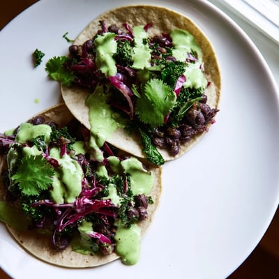 Crispy corn tortillas loaded with smoky black beans wilted kale and vibrant green sauce