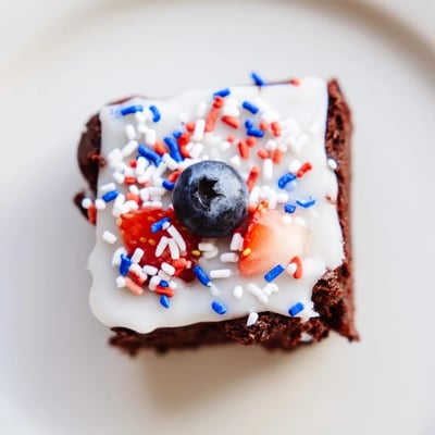 Bite-sized brownie bites glazed with white icing and colorful Fourth of July decorations for summer parties.
